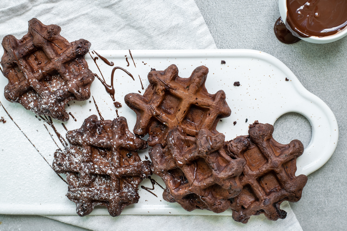 Bovenaanzicht van 5 chocoladewafeltjes, op een wit keramieken plankje, op een lichtgrijze stenen achtergrond.