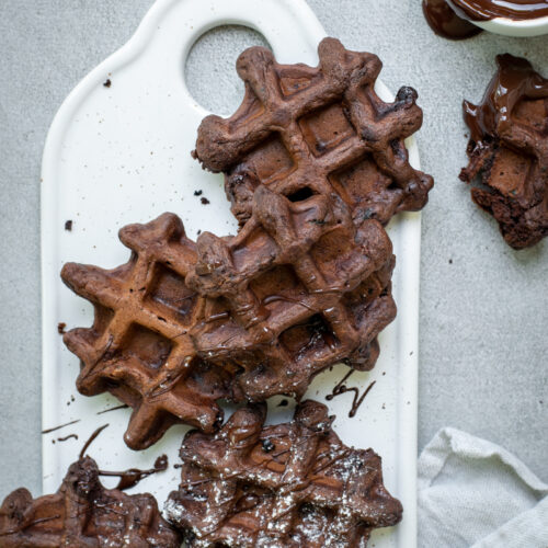 Bovenaanzicht van 5 chocoladewafeltjes, op een wit keramieken plankje, op een lichtgrijze stenen achtergrond.